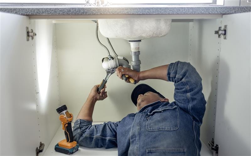 Plumber repairing pipes beneath a bathroom sink in Riverside